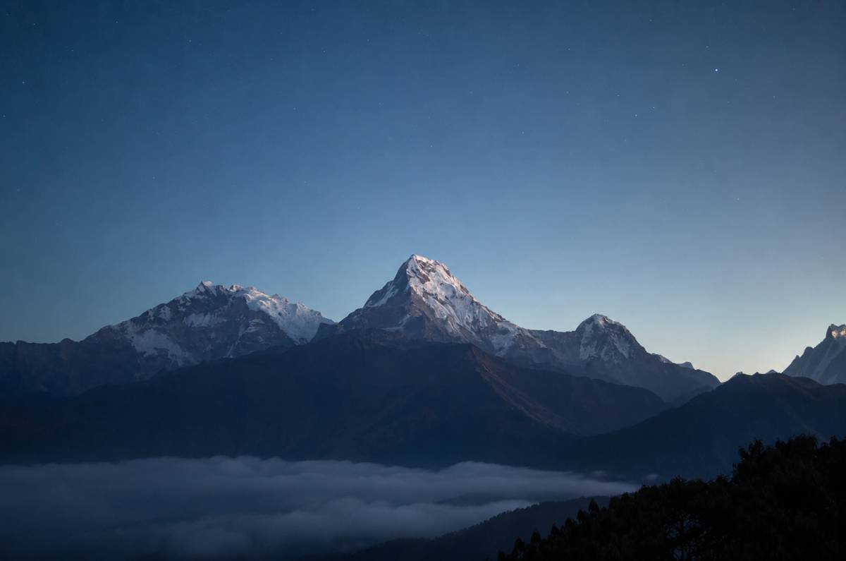 A towering snow-capped Himalayan mountain peak rising above a thick sea of fog under a clear, starry twilight sky.