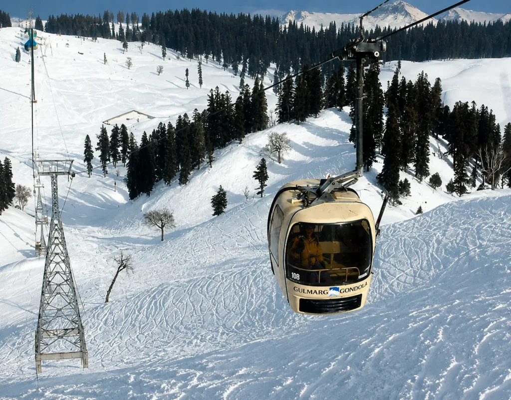 Gulmarg Gondola cable car passing over snow-covered ski slopes in Kashmir with Himalayan mountains in the background.