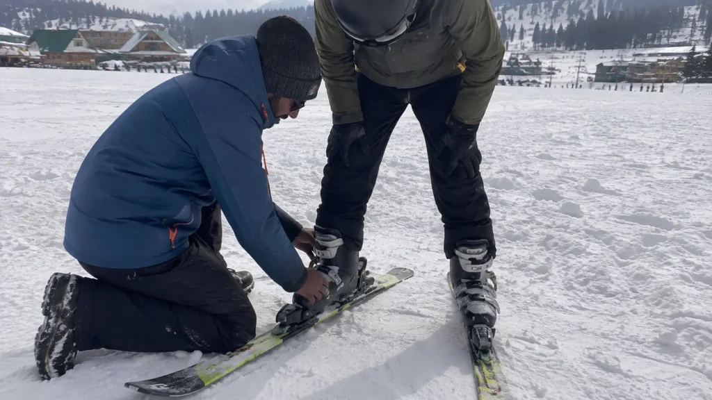 An instructor helping a student lock their boots into skis in Gulmarg